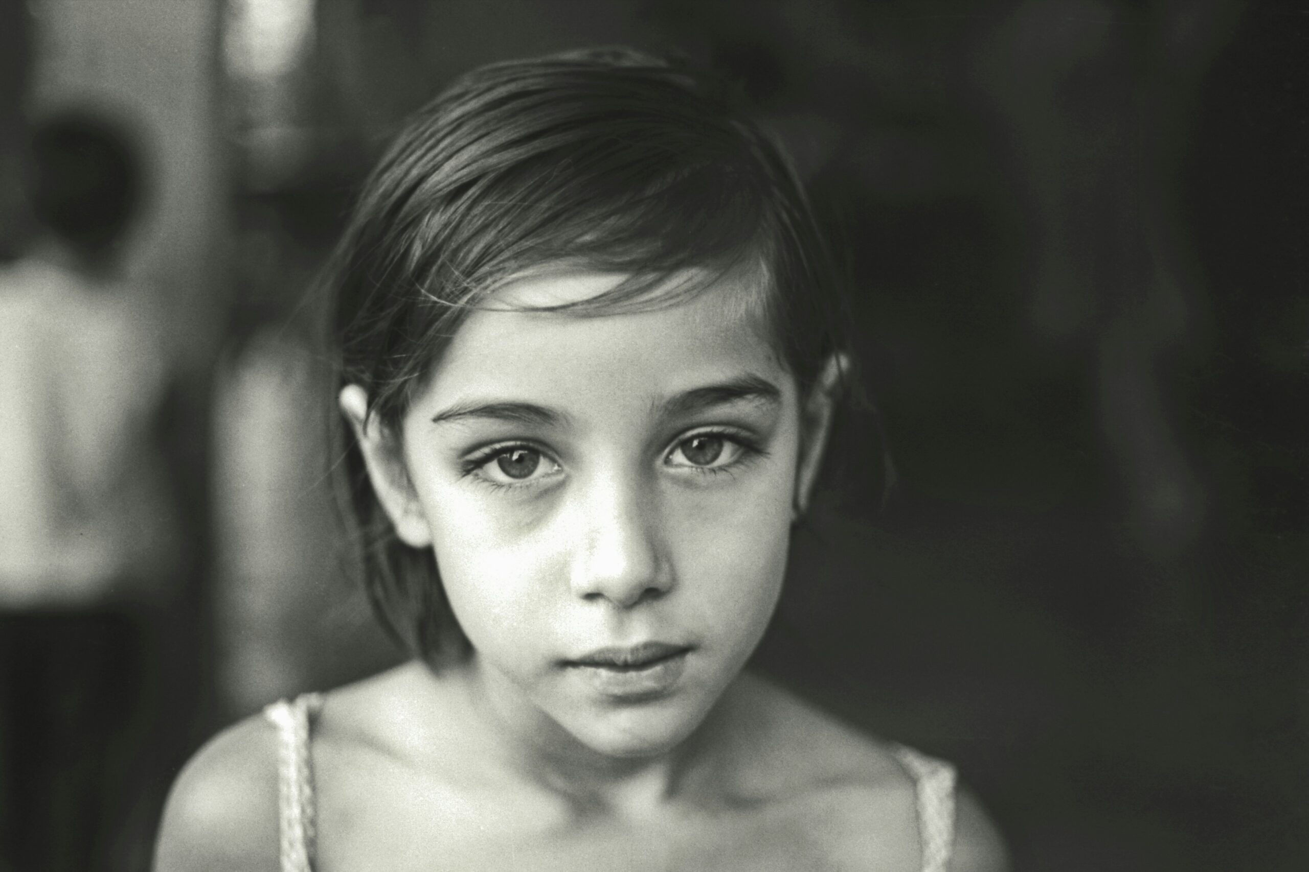 Close-up black and white portrait of a young girl with a somber expression, representing the face of a fatherless child.