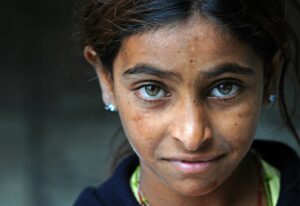 Close-up portrait of a young girl with striking light-colored eyes and a slight smile, representing the resilience of orphaned children.
