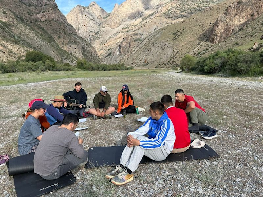 A group of young men sitting together on mats in a mountainous valley in Tajikistan for a Christian ministry gathering.