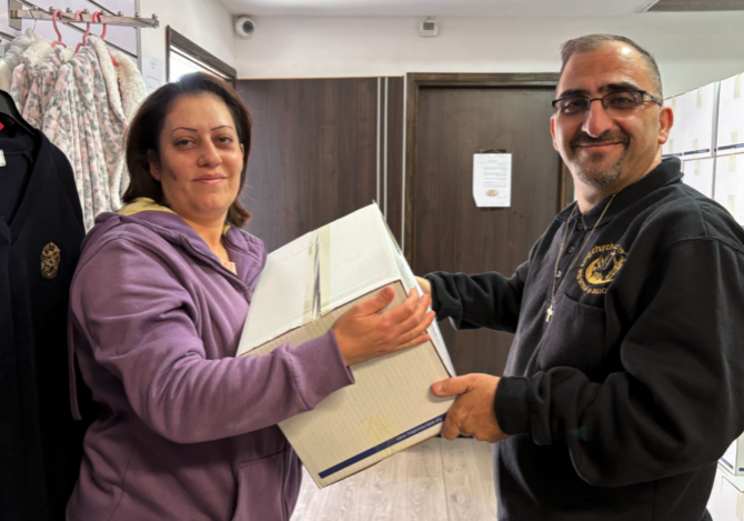 A man smiling while handing a large box of relief groceries to a woman in Nazareth.